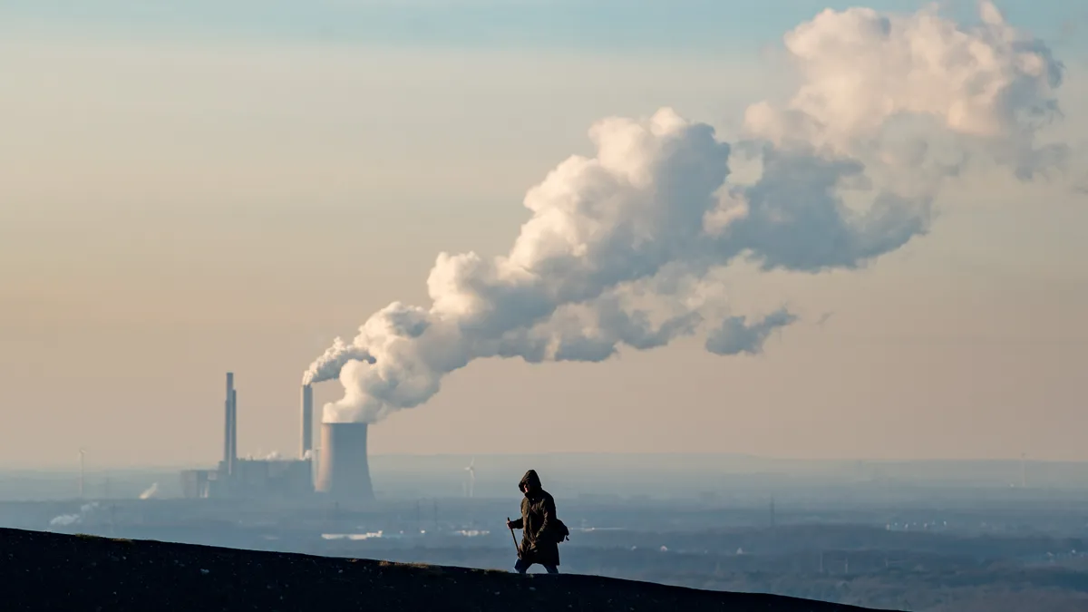 A lone hiker walks in the foreground while in the background steam and exhaust rise from a power plant on a cold winter day in Oberhausen, Germany.