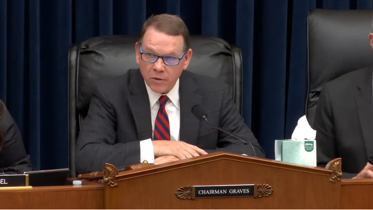 A seated man in a dark suit at desk with a nameplate reading "Chairman Graves."