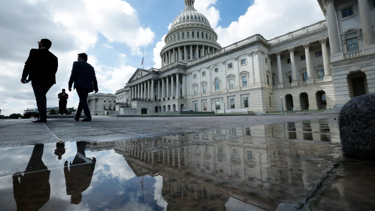 Two people in suits walk past the U.S. capitol building on a cloudy day.