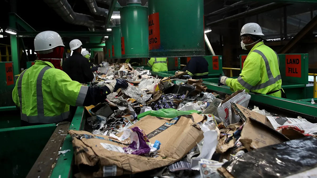 Workers sort recyclables by hand as they move down a conveyor belt at a recycling center.