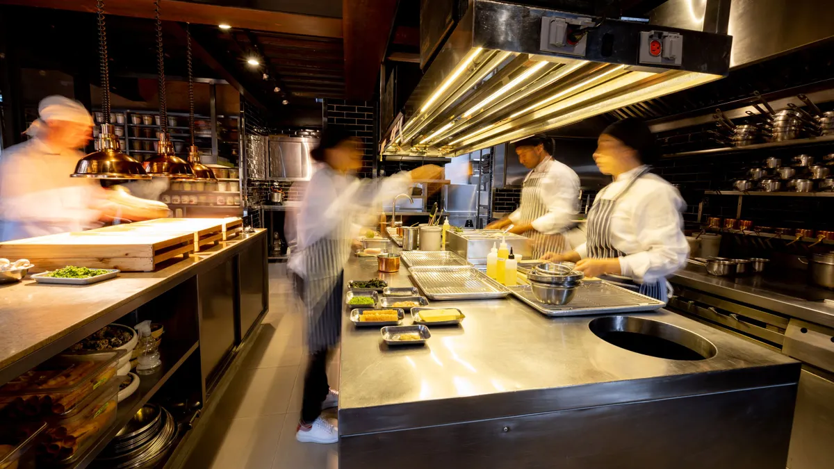 An image of back-of-house workers preparing meals in a kitchen. Their faces are blurred