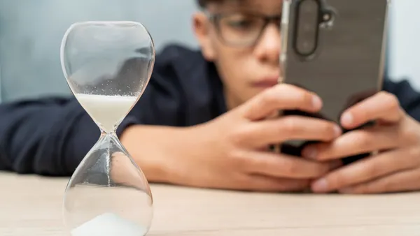 A teenager using a cell phone while ignoring an hourglass showing time running out.