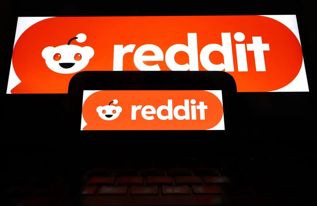 The Reddit logo is displayed on a cell phone and computer monitor.