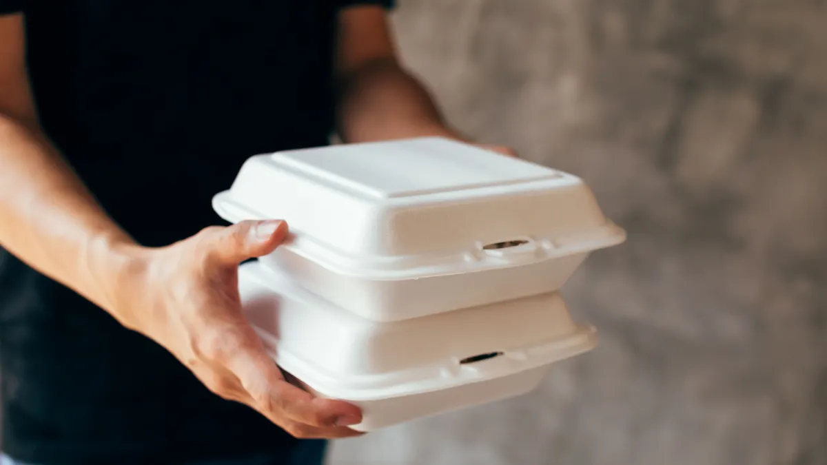 Hands carry styrofoam takeout containers