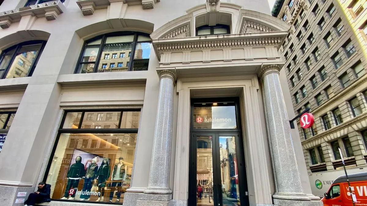 A person sits outside in the corner of a big store window looking at a mobile phone.