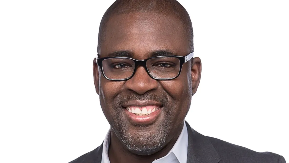 A headshot of a person wearing a gray suit and black glasses smiling.