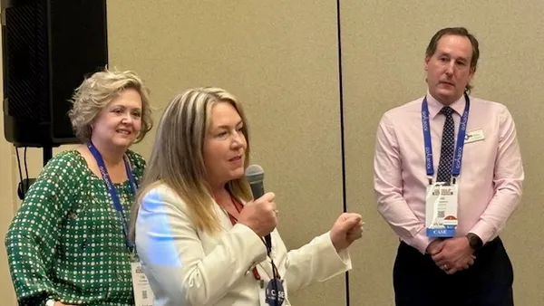 Three people are standing in a room. The person in the middle is holding a microphone