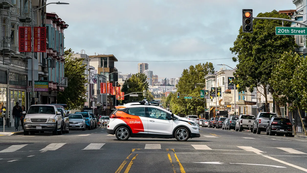 An range and white Chevy Bolt EV robotaxi operated by Cruise crosses an intersection San Francisco.