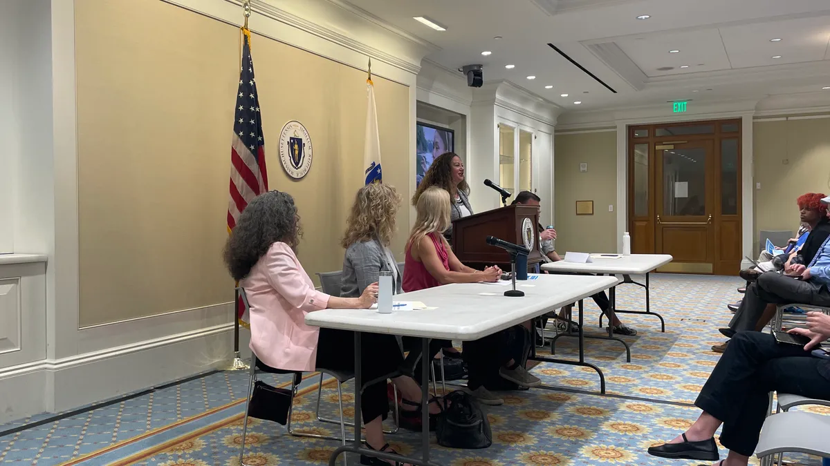 Person speaking at podium, in front of Massachusetts state seal