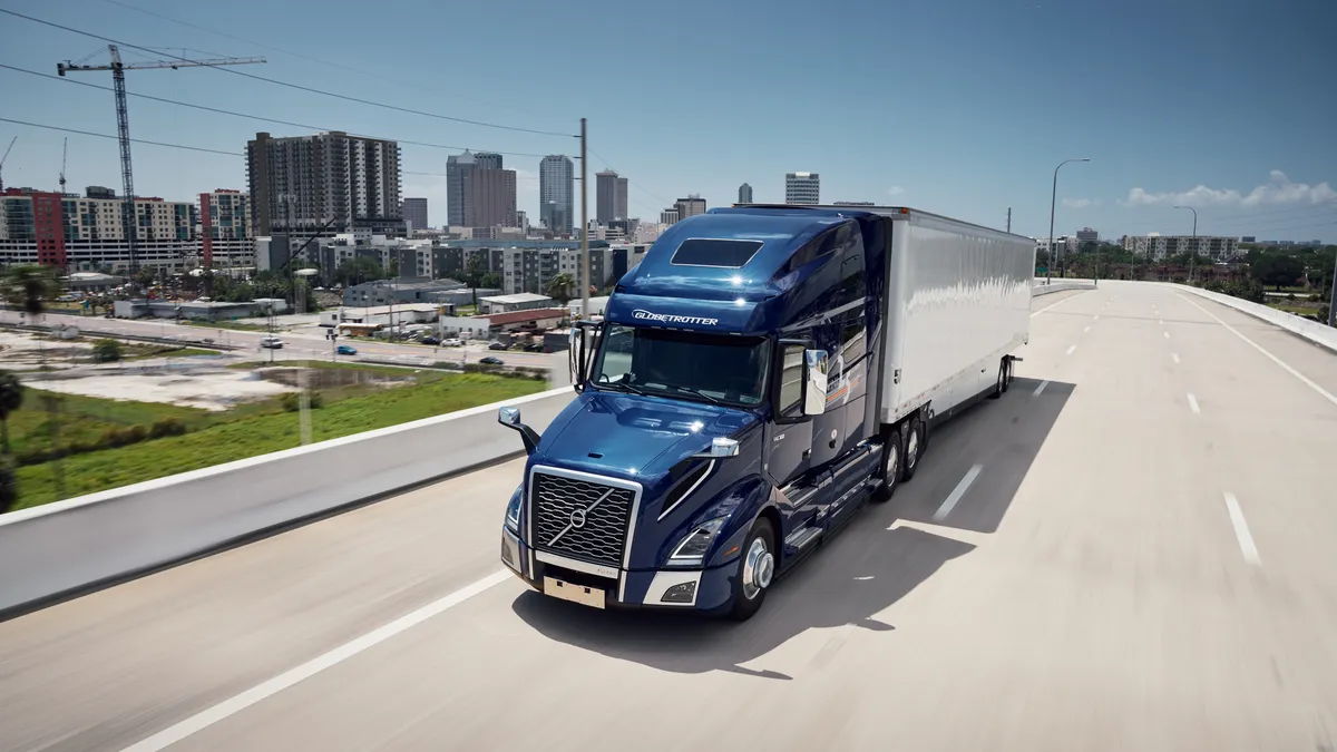 A Volvo VNL on an overpass with city buildings in the background.