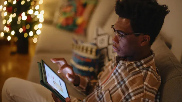 Person sits on a couch shopping on an iPad next to a Christmas tree.