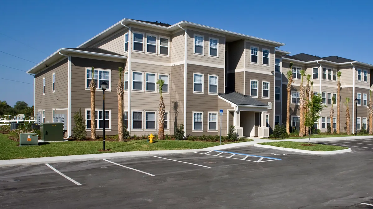 A three story apartments with palm trees outside on a blue sky sunny day.