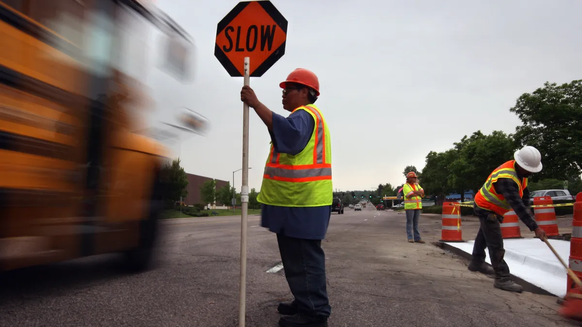 A construction worker holds directs traffic and holds a sign that says "SLOW."