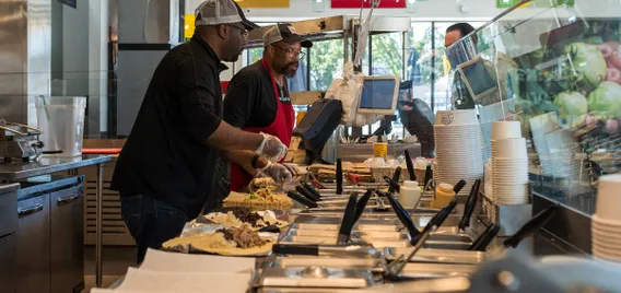 A photo of two employees at a makeline preparing food.