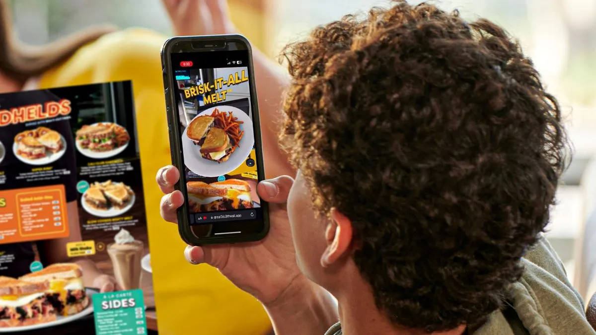 A photo of a guest viewing an augmented reality experience on Denny's menu.