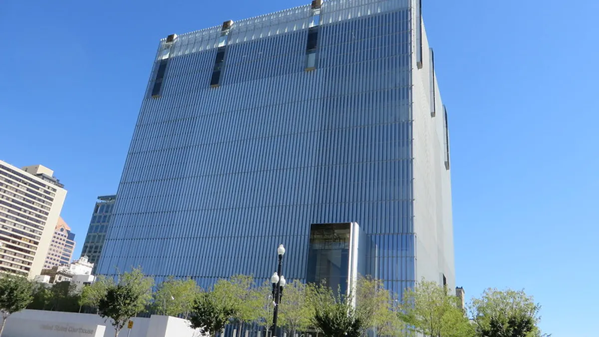 A tall, square-shaped building full of glass windows is visible in the middle distance, in front of a bright blue sky.
