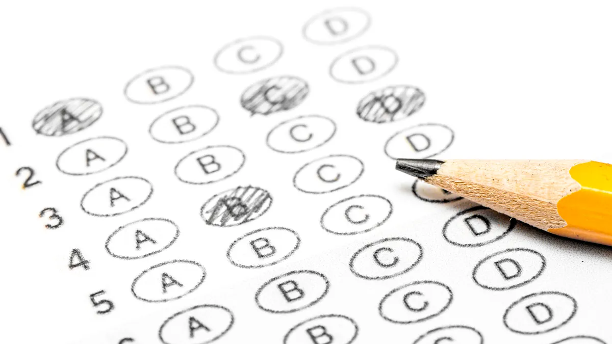 a white sheet of paper shows lines of bubbled letters to mark answers for a test. A yellow pencil rests on the paper.