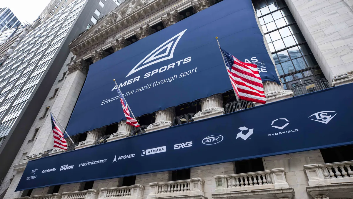 A blue Amer Sports banner hangs on a building, with American flags blowing.