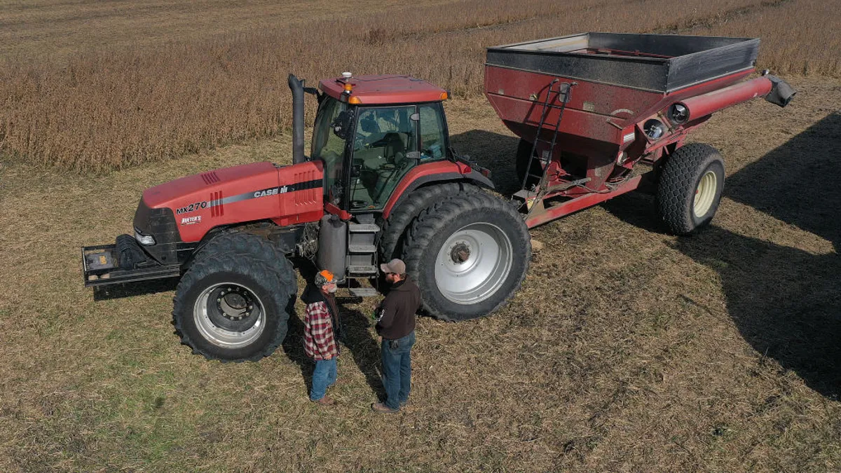 Two men stand in front of a tractor to talk.