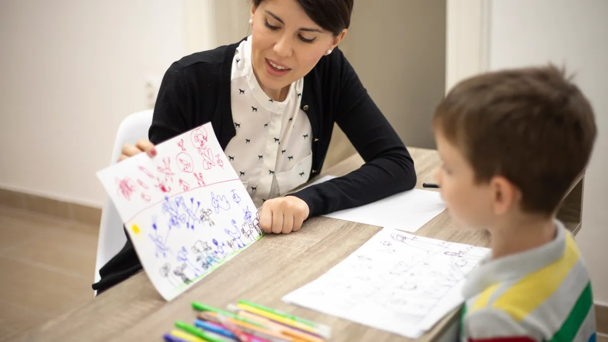 A woman therapist is shown discussing drawings with a young boy.