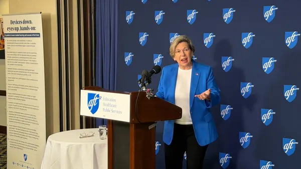 A person stands at a podium with behind a blue background with the American Federation of Teachers logo on it.