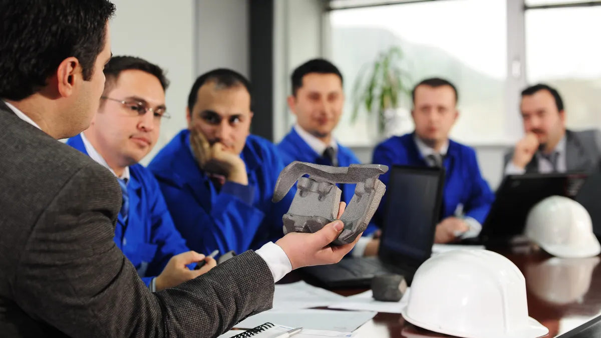 A man displays displays a component around a conference table.