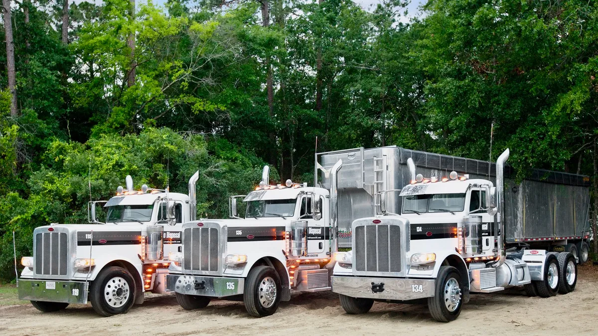 Three heavy duty trucks in a parking lot, trees in background