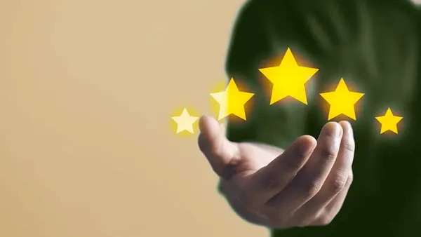 A hand outstretched against a beige background, holding five glowing yellow stars, symbolizes quality and excellence. The mood is uplifting and positive.