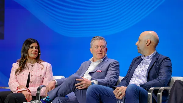 man speaks on a panel flanked by a man and a woman