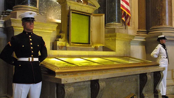An honor guard stands next to a display case containing the Declaration of Independence, Constitution and BIll of Rights.