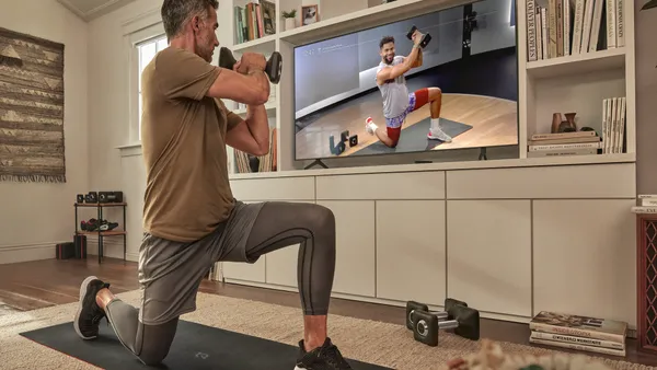 Person in athletic gray shorts and tights holds a dumbell weight while looking at TV