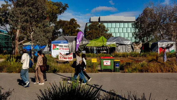 Tents situated on a college campus behind a walkway with people.