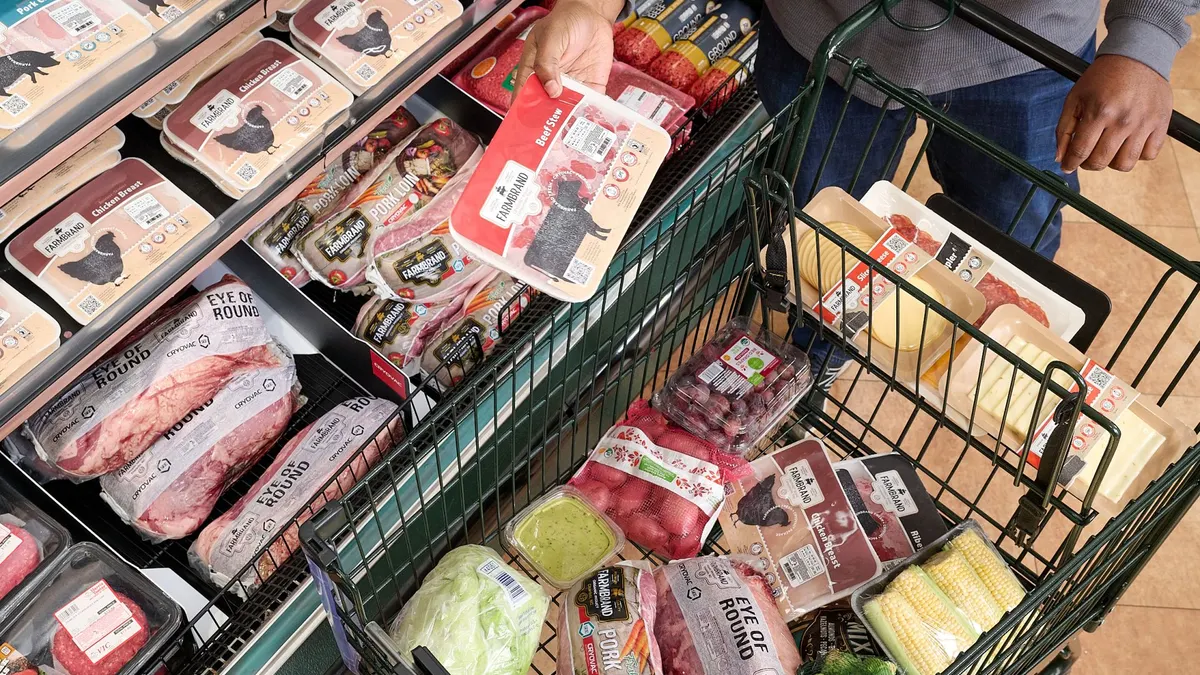 A person holds a package of meat in a grocery aisle with other types of packaged meats.