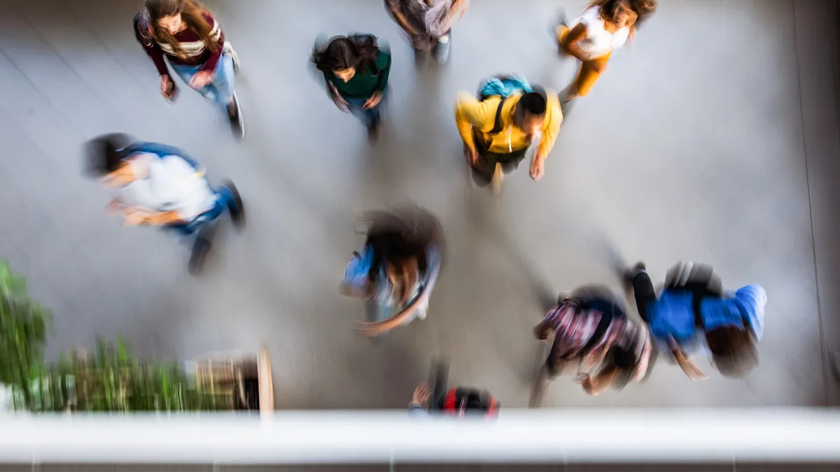 An aerial photo of blurred people in motion in a large open inside area. Some people are wearing backpacks