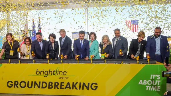 Large group of men and women at a table with confetti flying above them. Sign on table reads Brightline West.
