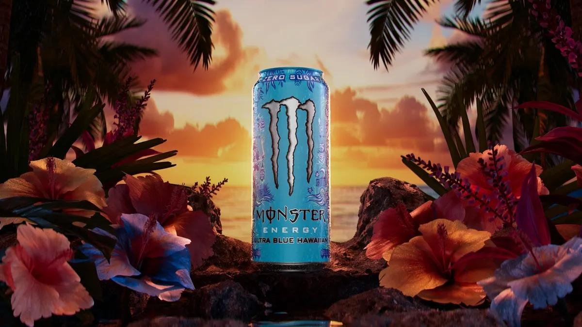 A photo of a can of energy drink on a rock near the ocean with tropical plants on both sides. The can says Zero Sugar Monster Energy Ultra Blue Hawaiian.