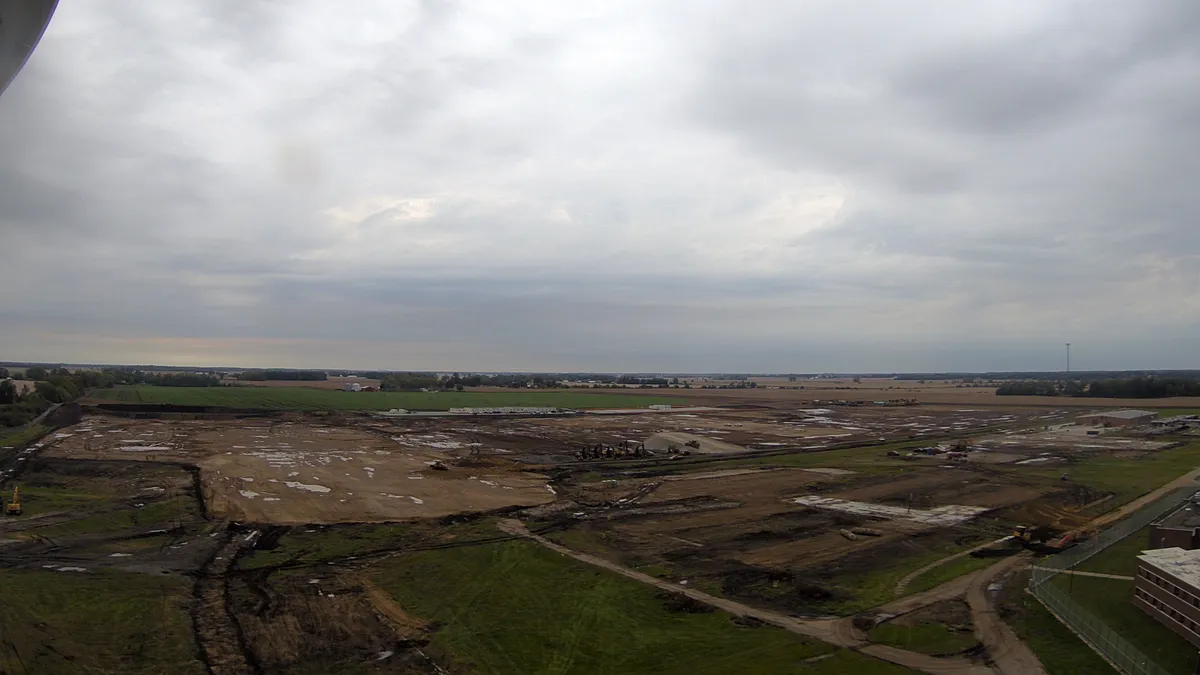 An empty, turned plot of land that's seen significant work. There are mounds of green space, but also churned dirt, framed against a cloudy sky.