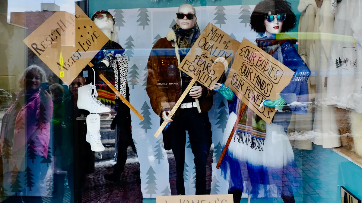 A resale boutique window features mannequins wearing secondhand clothing and holding handwritten signs touting civil rights.