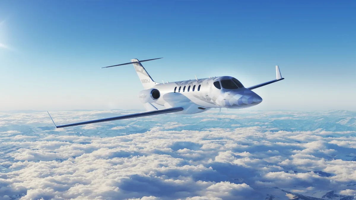 A reflective white and gray jet flying above the clouds with the blue sky in the background.