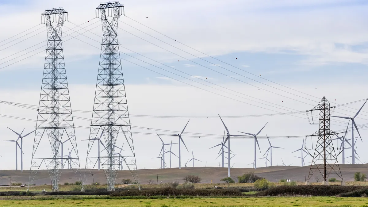 High voltage electricity towers and lines crossing the Sacramento-San Joaquin Delta; Wind turbines visible on the hills in the background; Solano County, Calif.