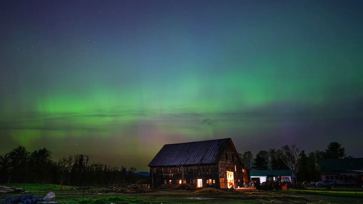 A farm is juxtaposed against a night sky with green and purple lights