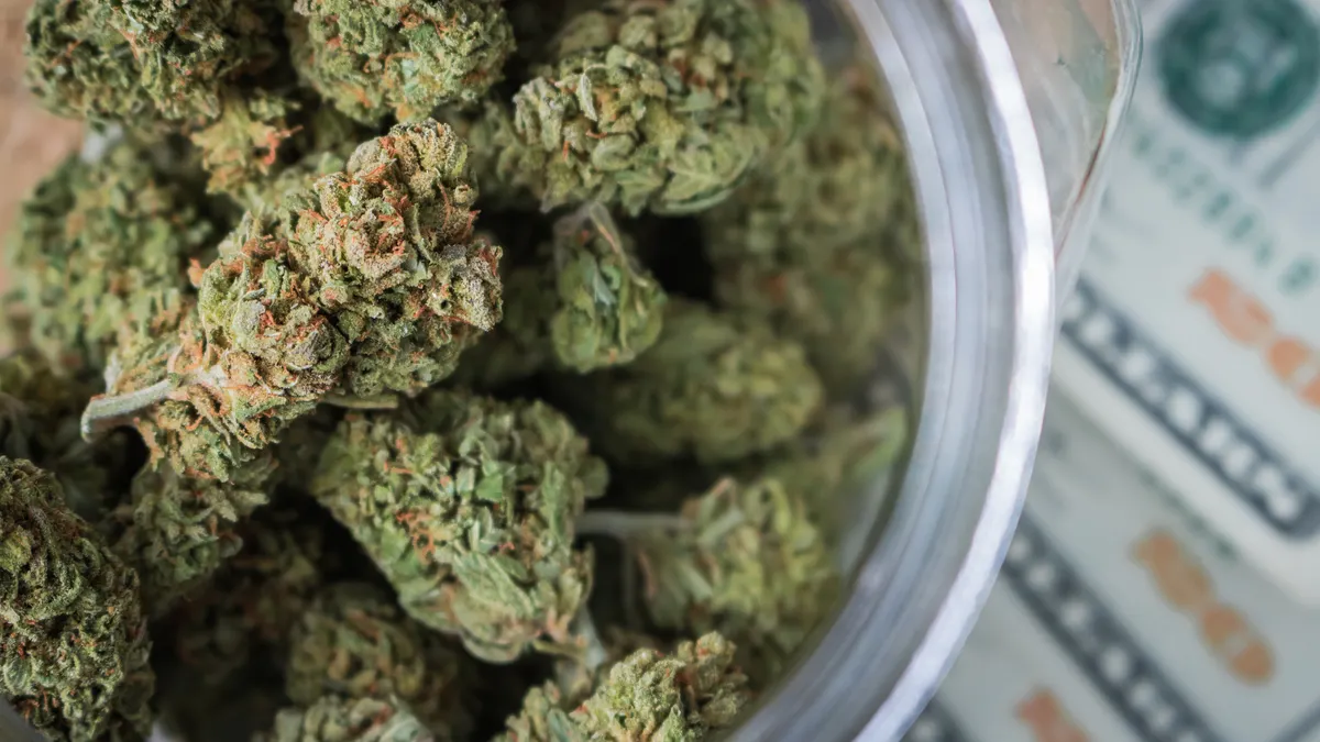 Looking down at marijuana buds in a round glass jar sitting on US paper currency ($20 bills).