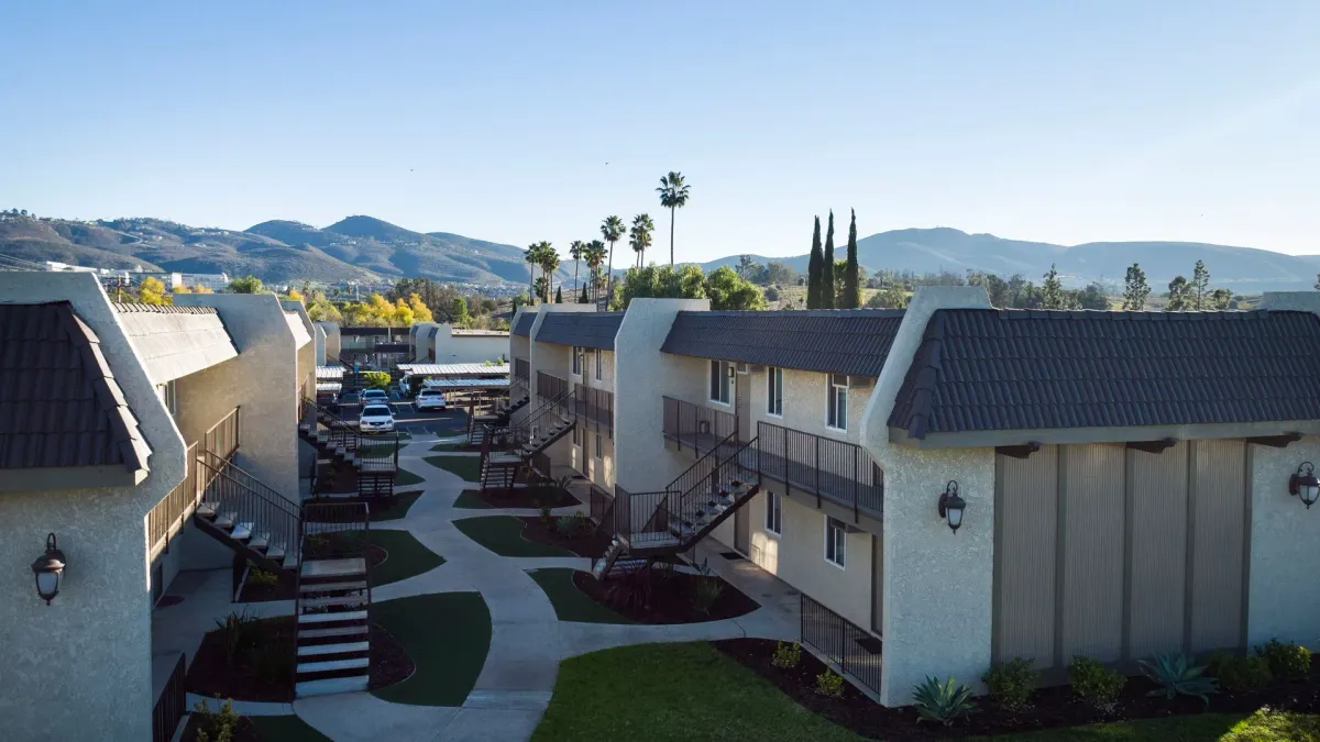 Two-level tan apartments with palm trees and mountains in the background.
