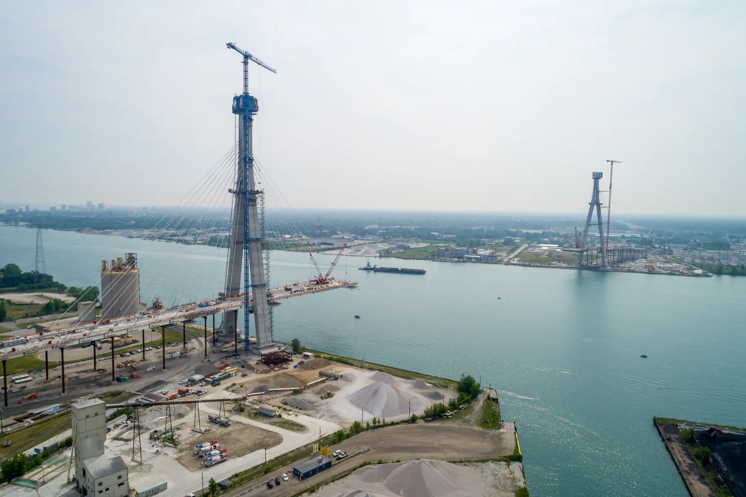 Two bridge towers on either side of a river stand tall, with scaffolding and cranes around them.