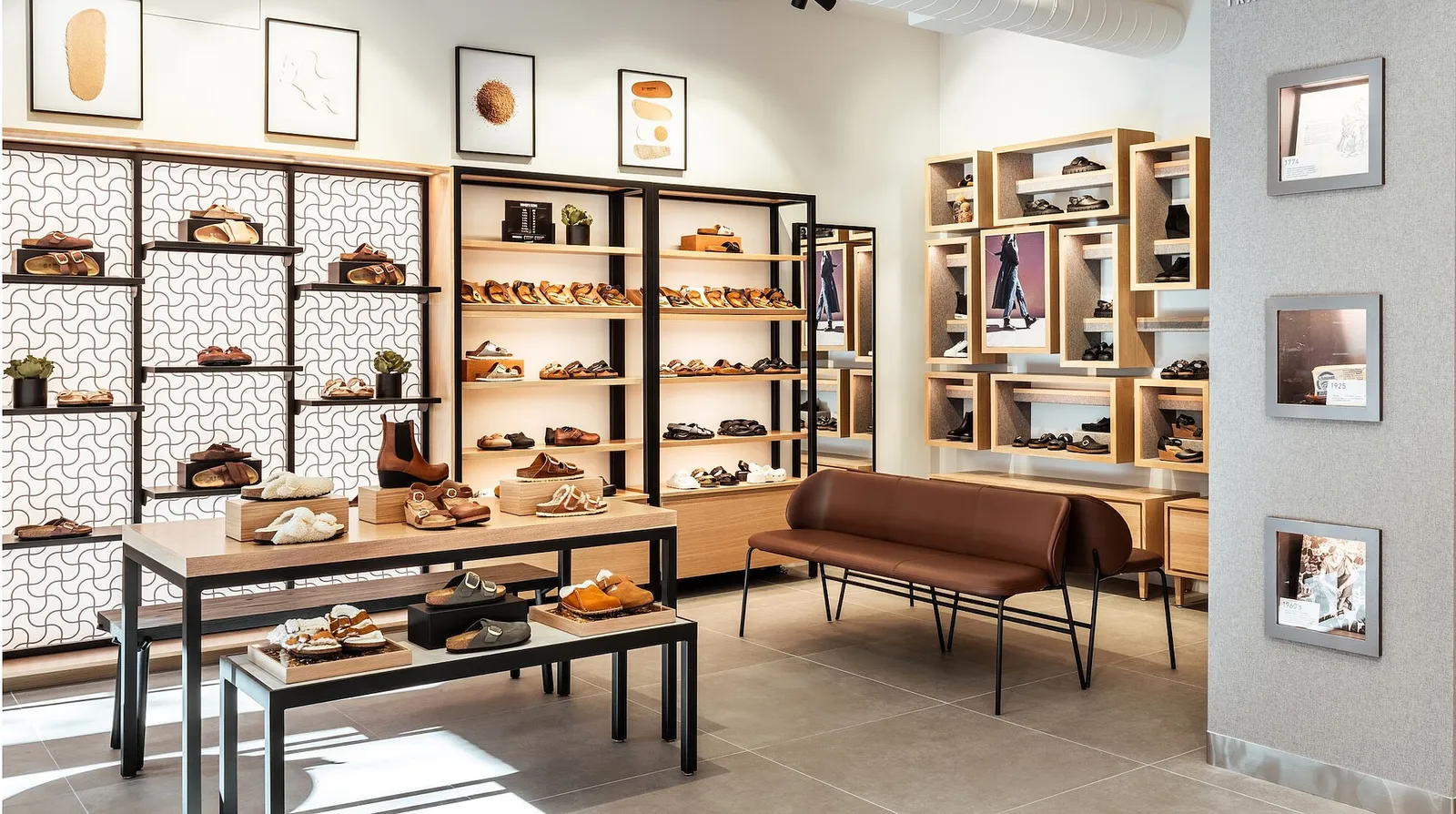 A display of Birkenstock shoes on a table, in front of a wall of Birkenstock shoes and a leather bench.