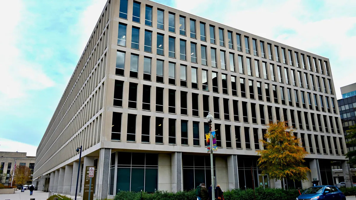 The outside of a building is seen. The building is concrete and has many windows