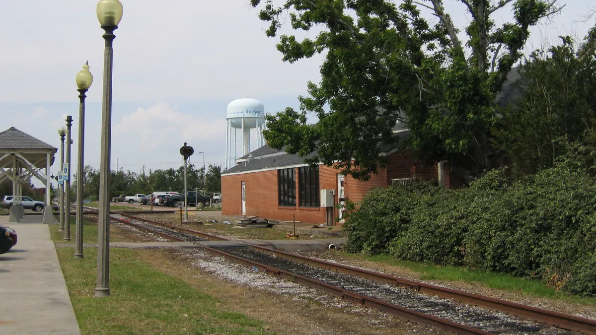 A single railroad track alongside a train station with streetlights and a water tank marked "Gulfport" in the background.