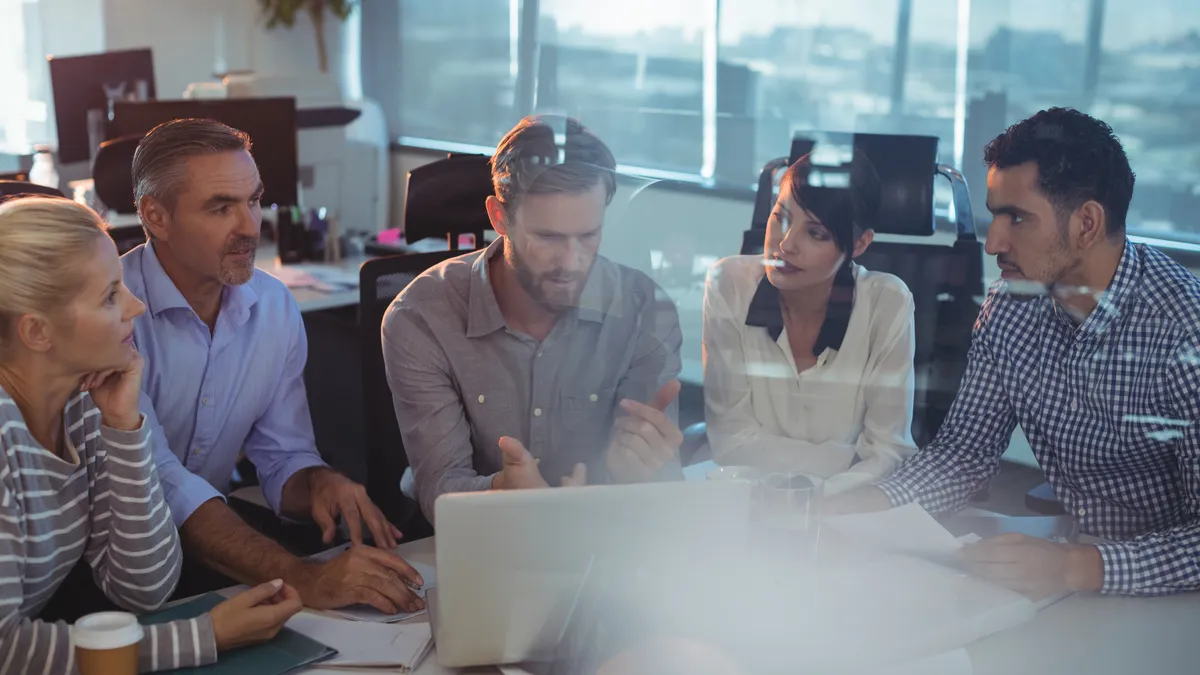 Business partners seen through glass discussing in meeting at office desk