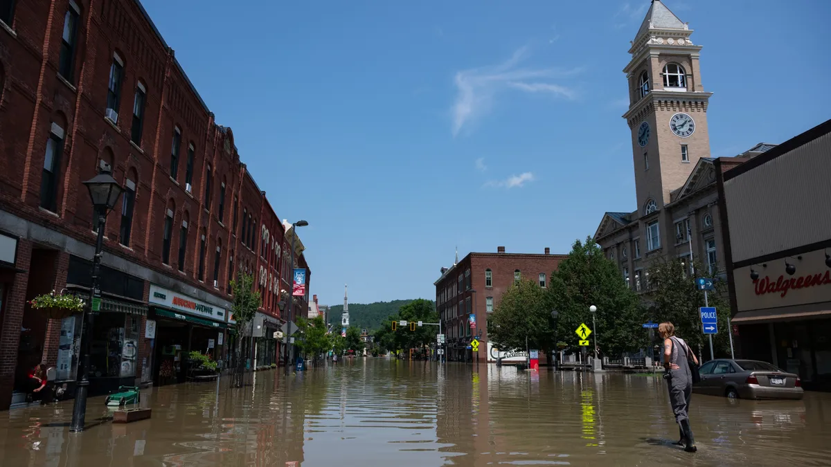 A main street in Vermont is flooded with one person wading through the water.