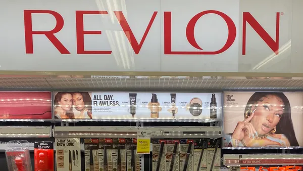 A large "Revlon" sign in red letters above a wall of cosmetics products in a drugstore.